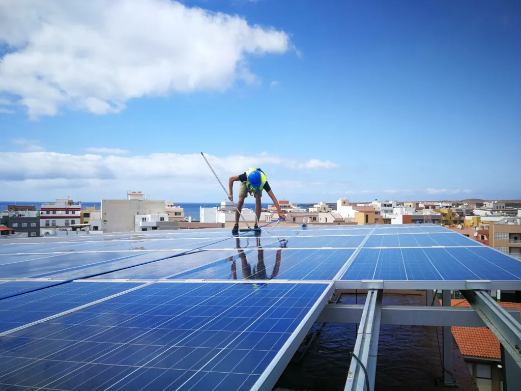 Técnico limpiando con pértiga los paneles solares de una cubierta con vistas al mar