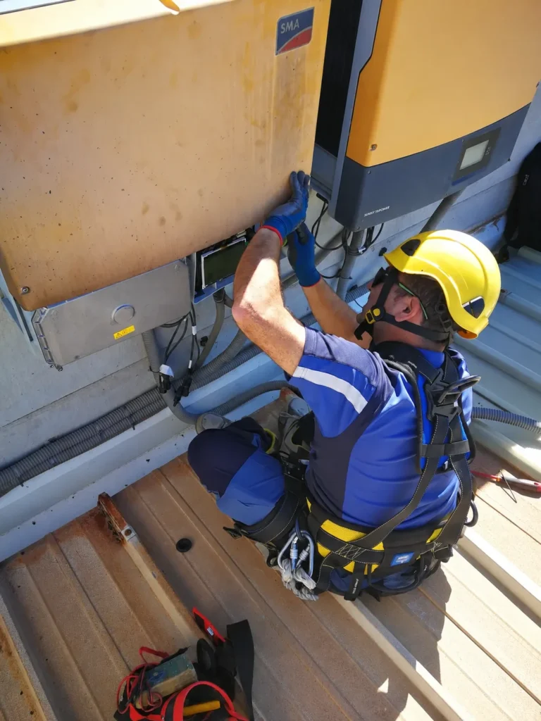 Técnico con casco y arnés revisando un inversor fotovoltaico en la cubierta de una instalación